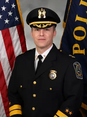 A photo of Police Chief Andrew McGurr in dress uniform in front of the American flag and a police flag.