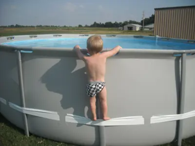 Photo from CPSC article demonstrating the hazard. A small child stands on a support strap and is able to reach over the edge of the pool. 